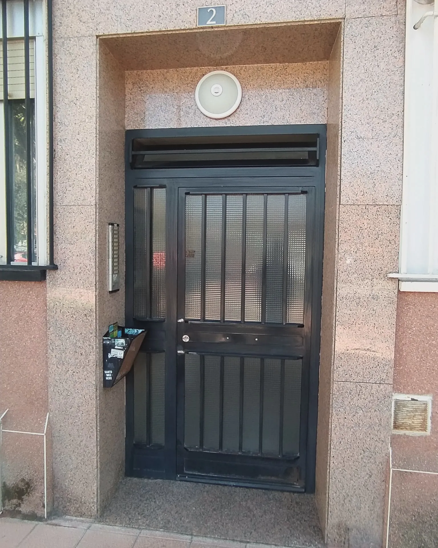 Puerta de portal metálica lacada en grafito sobre fachada de granito